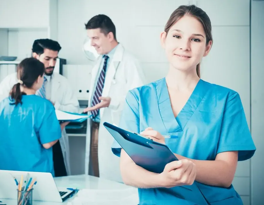 Medical assistant in hospital room with patient holding clipboard and smiling