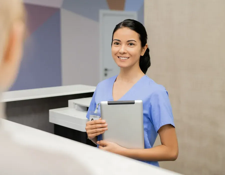 Medical assistant at front desk holding tablet smiling with patient